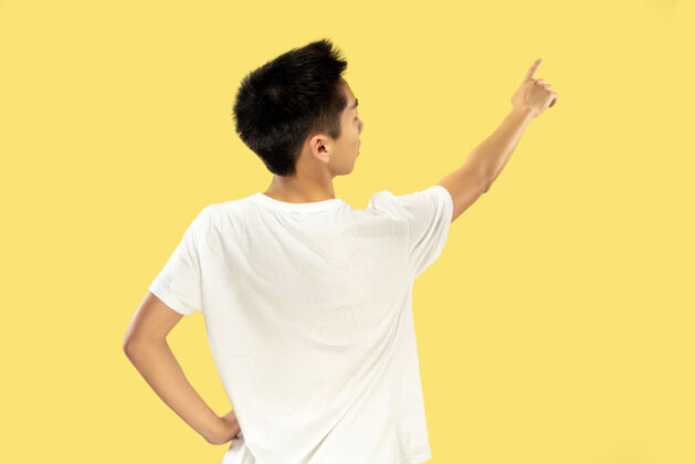 帅黄色工作室背景上的韩国年轻人半身像穿白衬衫的男模指向广告的地方人类情感的概念 面部表情流行的颜色工作人专业