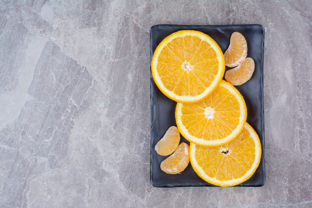 水果橘子和橘子片放在黑盘子里美味切片柑橘