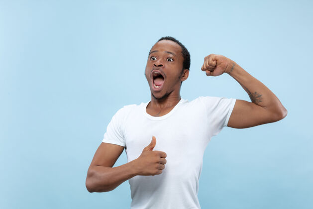 胡须半身特写 蓝色背景 身穿白衬衫的非洲裔美国青年人类情感 面部表情 广告 概念庆祝 惊讶 惊讶 震惊 疯狂的快乐就业非洲工作
