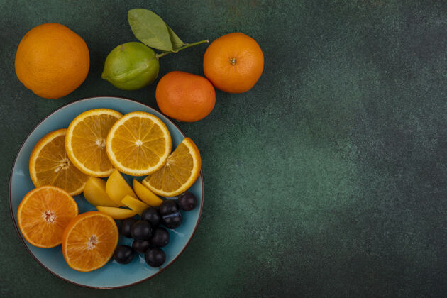 绿色顶视图复制空间橙色切片与甜樱桃在一个蓝色的盘子与橘子在一个绿色的背景甜味空间樱桃