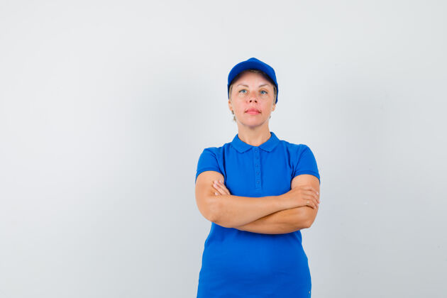 蓝色成熟的女人交叉双臂站在蓝色t恤里 看起来很严肃帽子严肃脸