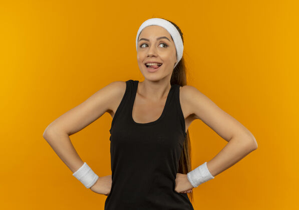市民身穿运动服 头戴头巾的年轻健身女士站在橙色的墙上 面带喜悦和积极的微笑看健身运动员