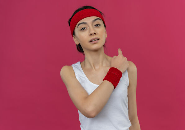 公民身穿运动服的年轻健身女士 头戴头巾 自信地向后指 站在粉红色的墙上头带女人运动员