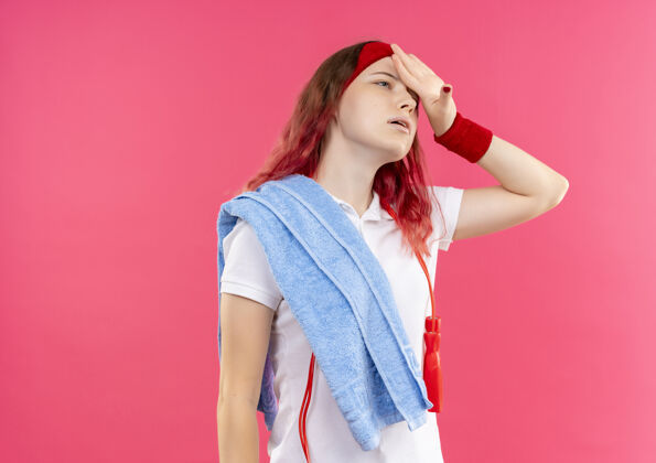 女戴着头巾 肩上扛着毛巾 站在粉红色的墙上 看上去疲惫而疲惫的年轻运动女性肩膀累运动装
