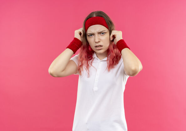 人戴着头巾的年轻运动女郎站在粉红色的墙上 脸上带着恼怒的表情表情烦恼人