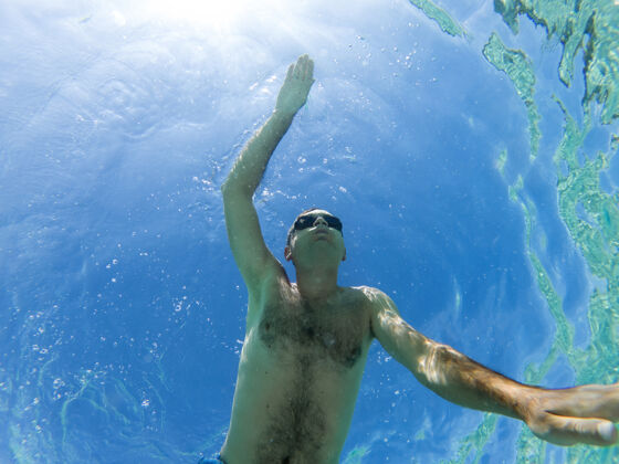 人高加索男子在水下游泳时戴着泳镜蓝色透明的水健身湿深