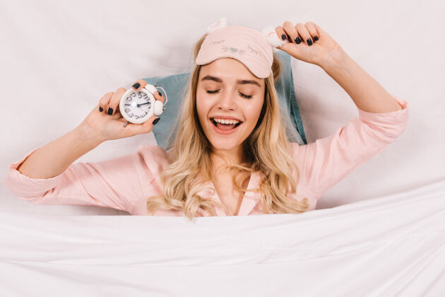 微笑一个戴着粉色睡眠面具的女人在床上摆姿势手舒适女性