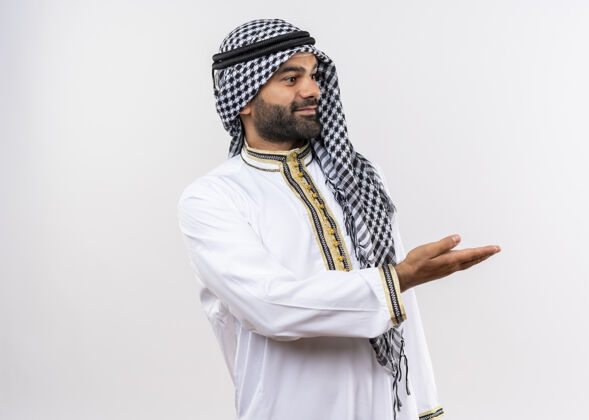 穿身着传统服装的阿拉伯男子站在白色的墙壁上 一边看着展示复制品的空间 一边高兴地看着人请公民