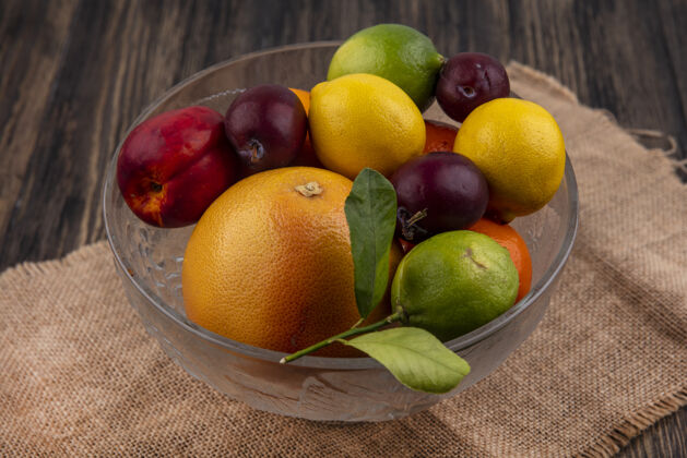 食物侧视图水果混合柠檬 酸橙 李子 桃子和橘子放在米色餐巾上的花瓶里米色混合餐巾