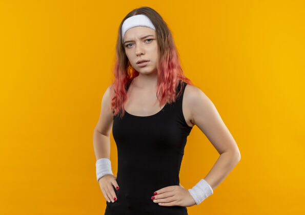年轻身着运动服的年轻健身女士站在橙色的墙上 表情自信严肃表情人表情