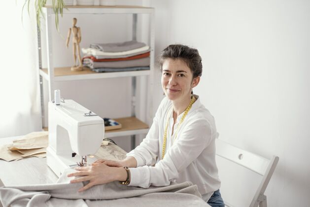 缝纫工艺女裁缝手拿缝纫机在工作室工作的侧视图女卧式服装