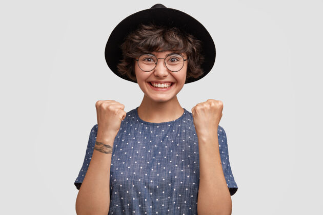 高兴快乐的白种人可爱的年轻女模特握紧拳头帽子水平眼镜