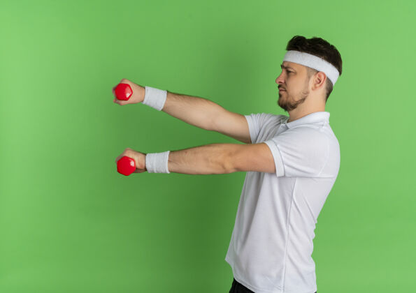人身穿白衬衫 头箍戴着哑铃的年轻健身男子站在绿色的墙上锻炼身体手势健身年轻人