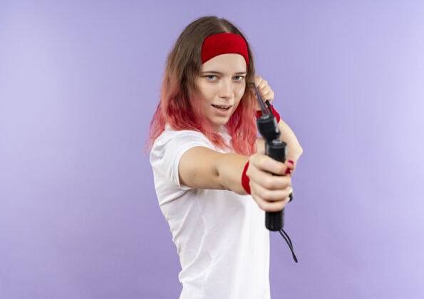 年轻人戴着头巾 手持跳绳瞄准紫色墙壁的年轻运动女性姿势站着跳跃
