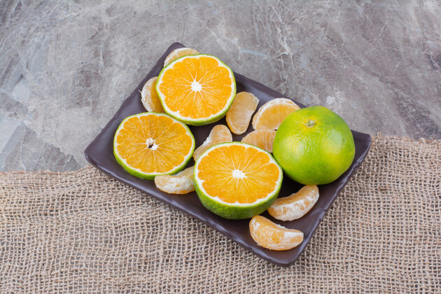 柑橘在石头背景上放一盘新鲜的橘子切粗麻布天然