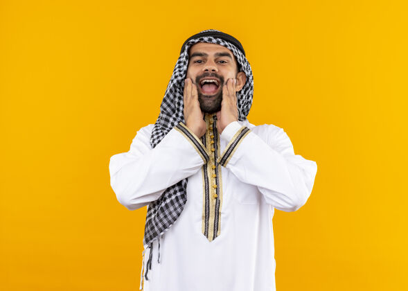 穿身着传统服饰的快乐阿拉伯商人站在橙色的墙上 微笑着微笑欢呼看