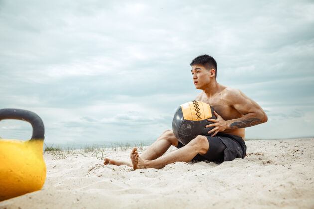 成人年轻健康的男子运动员在海滩上做深蹲交叉年轻健身