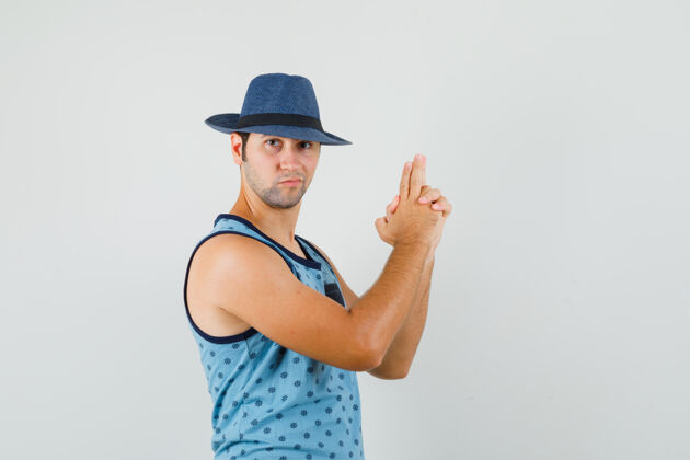 年轻一个年轻人穿着蓝色的背心 戴着帽子 摆着枪的姿势 看上去很自信前视图商人微笑时尚