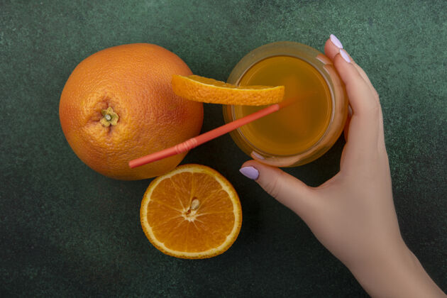 切片俯视图：一位女士手里拿着一杯橙汁 杯子里有一根红色的吸管和一片橘子 背景是绿色的葡萄柚视图红色吸管