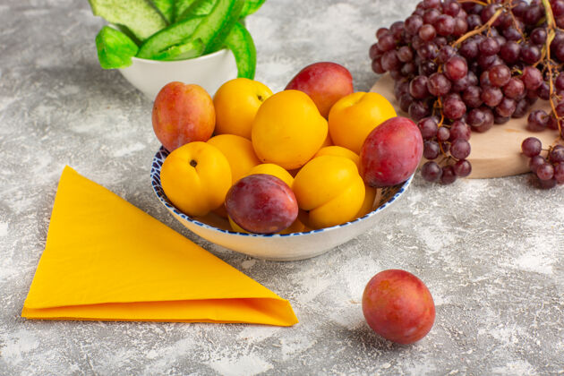 正面前视图新鲜甜杏黄色水果盘内与李子和葡萄在白色办公桌上新鲜可食用的水果办公桌