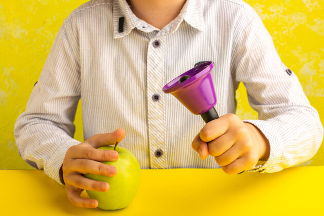 苹果正面图：黄色表面上拿着绿色苹果和紫色铃铛的小孩水果拿着小