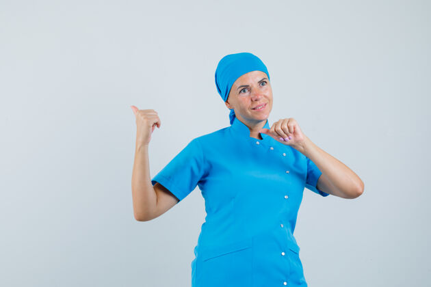 疾病穿着蓝色制服的女医生用大拇指指了指后面 看上去充满希望 正面视图肖像制服站立