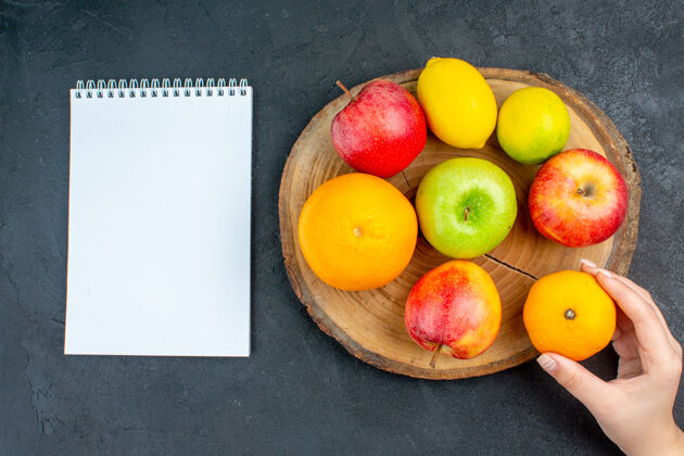 柑橘顶视图苹果柠檬橘子木板笔记本橘子在女人手上黑暗的表面观点苹果柠檬橙子柠檬