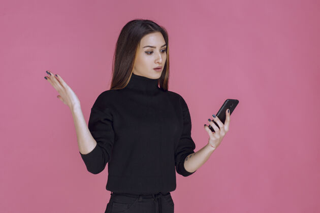 小工具穿着黑色毛衣的女人拿着智能手机发短信或查看社交媒体聊天休闲设备