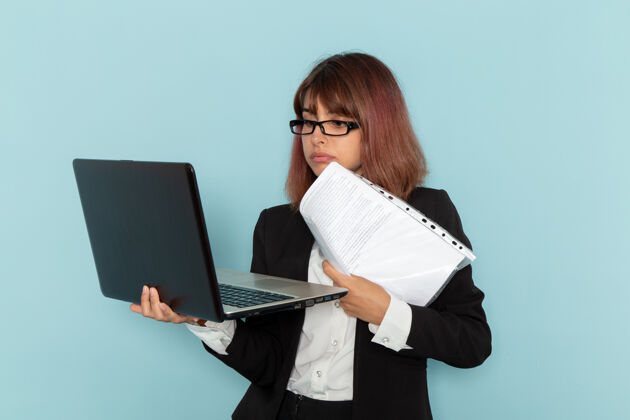 前正面图：身着正装的女上班族拿着文件和笔记本电脑在蓝色的表面上手持工作工作