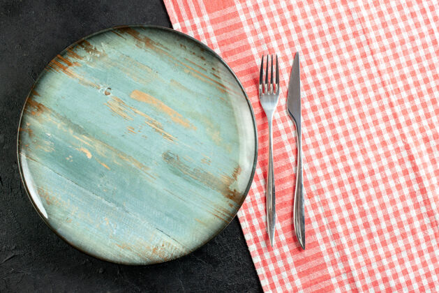 顶部俯视图：黑色桌子上红白格子桌布上的圆形餐盘刀叉烹饪视图器皿