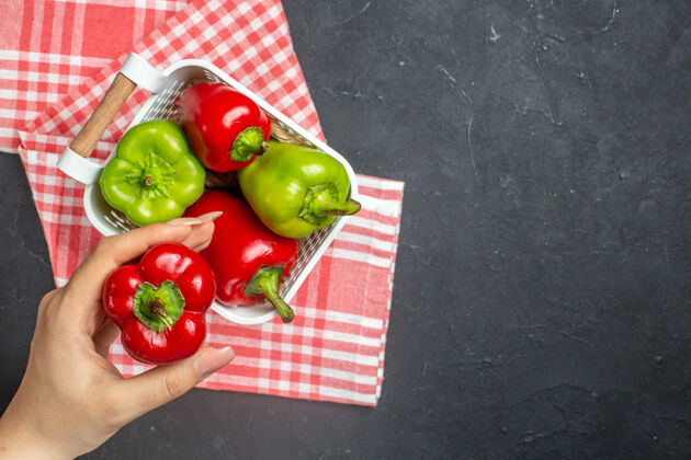 胡椒顶视图绿色和红色辣椒在塑料篮上红白格子桌布红色甜椒在女性手上黑色表面上自由空间篮子景观桌布