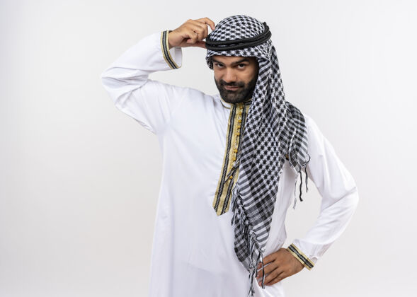 穿一个穿着传统服装的阿拉伯男人站在白墙上用手指搔头抓头手指