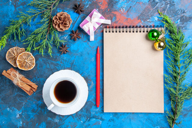 干燥俯瞰笔记本上的圣诞球松树枝桂枝八角干柠檬片一杯茶在蓝色的表面切片茶杯子