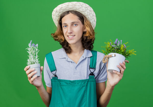 穿年轻的园丁 穿着连体衣 戴着帽子 手里拿着盆栽植物抱着植物帽子