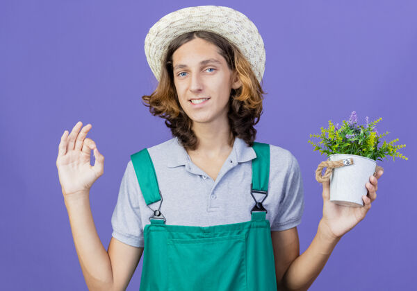 植物年轻的园丁 穿着连体衣 戴着帽子 微笑着捧着盆栽植物站着花园标志