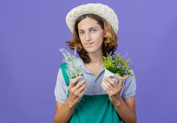 微笑年轻的园丁 穿着连体衣 戴着帽子 手里拿着盆栽植物锅连身衣花园