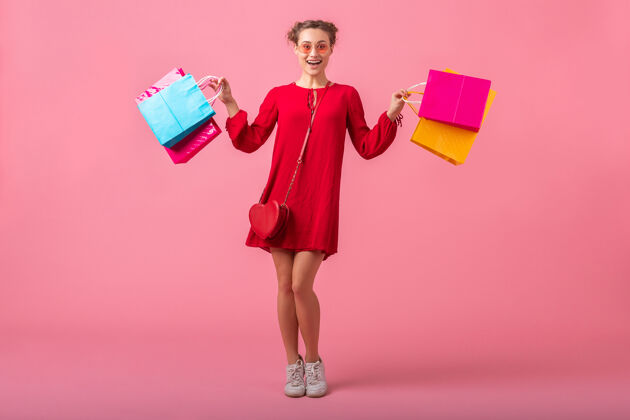 身高迷人快乐微笑的时尚女性购物狂身着红色新潮连衣裙手持五颜六色的购物袋贴在粉色的墙上 销售兴奋 春夏时尚潮流衣服购买长度