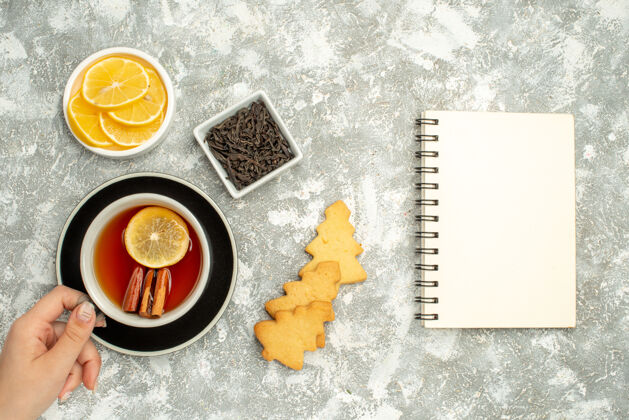 顶部俯视图一杯茶在女人手中饼干碗巧克力和柠檬片笔记本上的灰色表面茶杯视图饼干