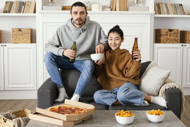 美好时光夫妻俩在室内喝啤酒吃零食看电视活动情侣