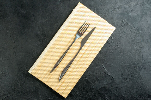 刀叉黑色桌子上米色木板上的顶视图叉和刀 有自由空间顶部衣夹视图