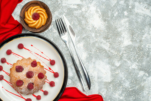 顶部俯瞰白色椭圆形盘子上的浆果蛋糕 红色披肩 灰色表面上的饼干叉和餐刀 复制空间早餐景观晚餐