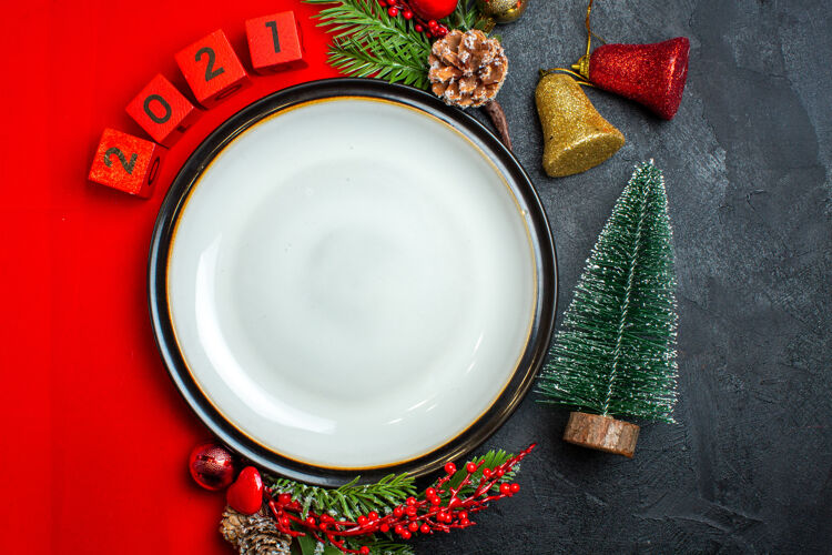 碗新年背景的垂直视图 带有餐盘装饰配件杉木树枝和数字 放在黑色桌子上圣诞树旁的红色餐巾上圣诞节搅拌碗树枝