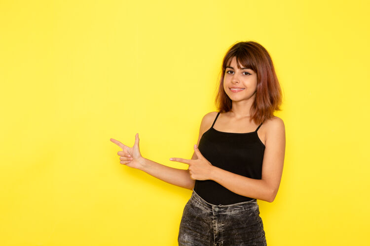 微笑身穿黑色衬衫和灰色牛仔裤的年轻女性在黄色墙壁上微笑和摆姿势的正面视图漂亮衬衫前面