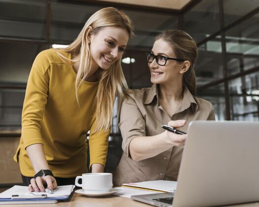 执行官两个微笑的女商人在办公桌旁用笔记本电脑工作女性员工商务女性