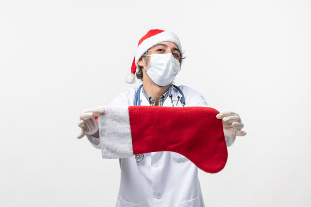 袜子正面图男医生举着白色墙壁上的大节日袜子病毒节日帽子圣诞节医生