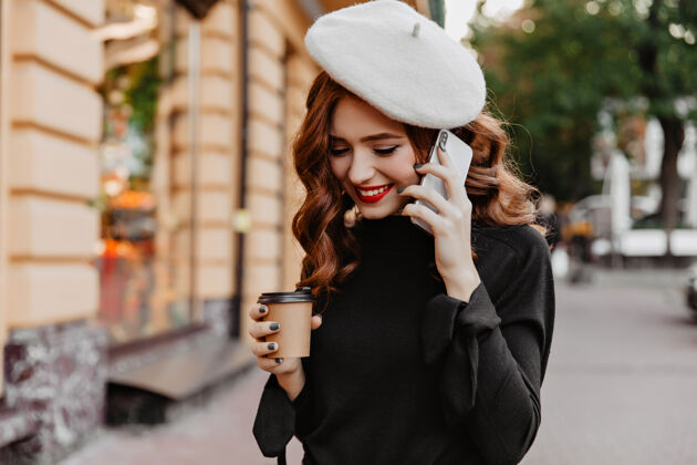 生姜可爱的女模特 姜黄色的卷发在打电话幽默的法国女士在街上和智能手机合影街道风格交谈