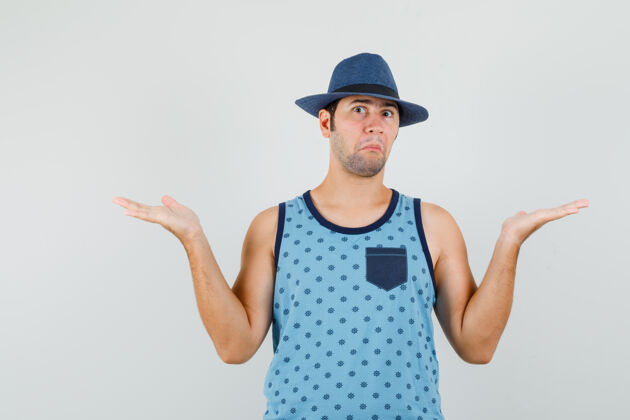 帽子一个穿着蓝色单品的年轻人 戴着一顶帽子 表现出无助的姿态 看上去很困惑男性困惑成功