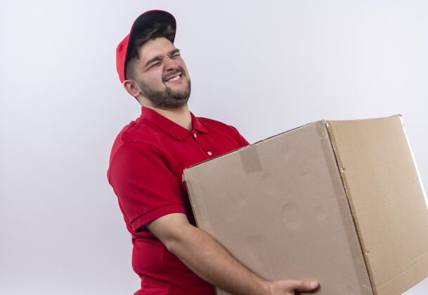 年轻年轻的送货员穿着红色制服 戴着帽子 手里拿着一个大纸箱 承受着沉重的重量重量帽子男人