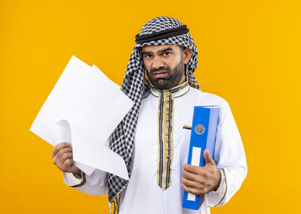 商务人士阿拉伯商人在传统的穿着夹和空白页不高兴和困惑站在橙色的墙上页面传统空白