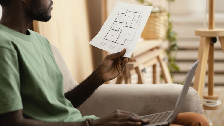 房子沙发上的男人正在计划用笔记本电脑重新装修房子的侧视图战略环保生活方式